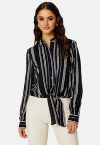 Zwart-wit gestreepte blouse die aan de taille is geknoopt, gemaakt van gladde stof met lange mouwen en een klassieke kraag.