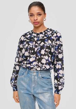 Blouse à motif floral en noir, bleu et blanc ; elle dispose d'un col plissé, de longues manches et est associée à un jean bleu clair.