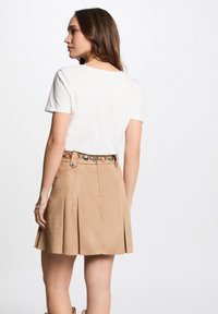 T-shirt bianco a maniche corte abbinato a una gonna plissettata beige con una cintura decorativa e dettagli metallici, visto da dietro.