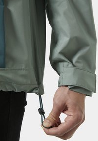 Lichtgroene waterdichte jackmanchet met een trekkoord. Gladde textuur en een aansluitend ontwerp. Verstelbare togglehardware voor het aansnoeren.