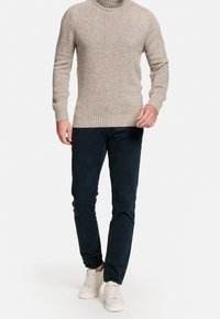 Světlý béžový pletený rolák s žebrovanými manžetami a lemem, doplněný tmavě modrými úzkými kalhotami a bílými teniskami. Hladká struktura.