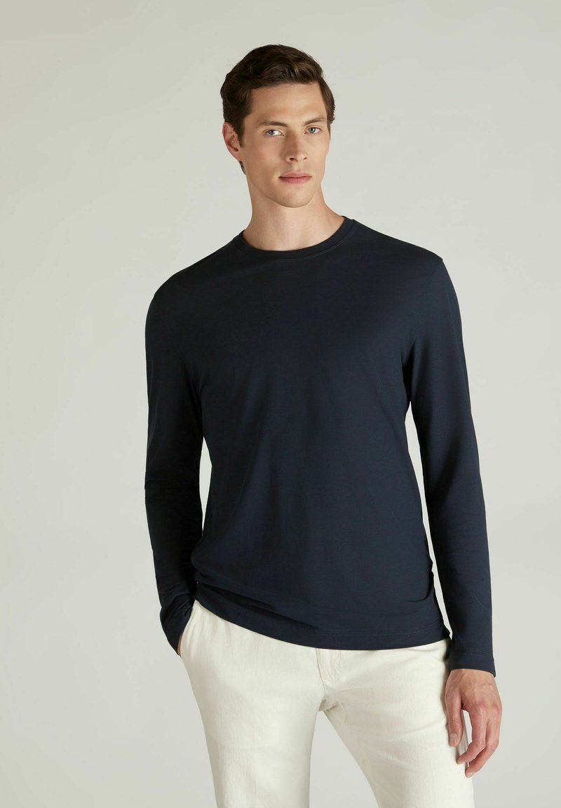 Chemise à manches longues marine en tissu léger, avec un col ras du cou et une coupe ajustée, associée à un pantalon de couleur claire.