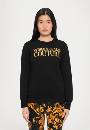 Black sweatshirt made of cotton with embroidered "VERSACE JEANS COUTURE" in gold. Features a crew neck and ribbed cuffs. Paired with patterned pants.