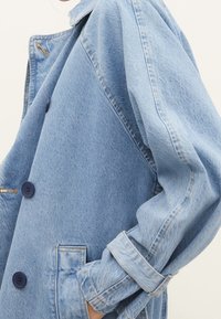 Ljusblå denimjacka med en avslappnad passform, som har två knappar fram, en patchficka och uppvikta ärmar. Texturerad tyg med subtila variationer.