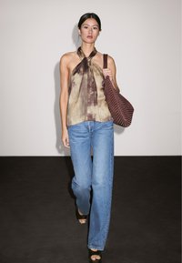 Beige a hnědé abstraktní vzorované halter top spárované s světle modrými širokými džínami. Modelka drží texturovanou burgundskou kabelku. Černé podpatky.