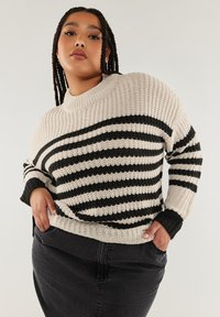 Randig stickad tröja i beige och svart, med breda horisontella ränder och hög krage. Strukturerat mönster med ribbade ärmslut.