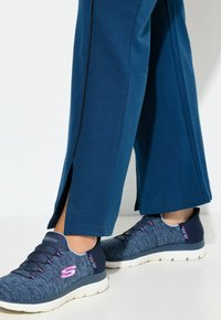 Niebieskie spodnie sportowe z bocznymi rozcięciami w połączeniu z granatowymi teksturowanymi butami sportowymi z różowymi akcentami i białymi podeszwami.