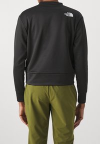 Felpa nera con maniche lunghe, colletto a giro e orlo a coste. Presenta un logo bianco sulla parte superiore della schiena; abbinata a pantaloni verdi.
