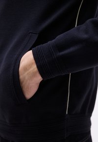 Χέρι εισάγεται στην μπροστινή τσέπη σκούρου ναυτικού φούτερ με ριμπ μανσέτες και ανοιχτόχρωμες πλευρικές ραφές.