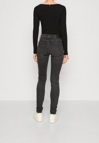 Una camiseta negra de manga larga combinada con unos jeans de mezclilla gris de corte ajustado. Los jeans tienen bolsillos traseros y un ligero desgaste. Unas zapatillas blancas casuales completan el look.