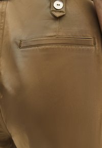 Bruine, gladde stoffen broek met een enkele achterzak en een knoopsluiting; heeft schone stiksels en een strak ontwerp.