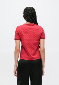 Czerwona koszulka z krótkim rękawem z delikatnym wzorem. Posiada okrągły dekolt i prążkowane mankiety. Materiał jest gładki, a krój luźny.