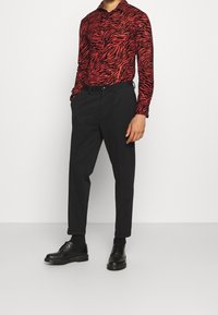 Camicia a righe rossa e nera con maniche lunghe, abbinata a pantaloni neri a sigaretta e scarpe nere con lacci.
