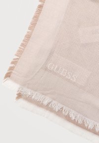 Μπεζ υφαντό ύφασμα με διακριτικό ριγωτό σχέδιο, φουντωτές άκρες και απαλό ανάγλυφο λογότυπο "GUESS" κοντά στη γωνία σε ανοιχτό φόντο.