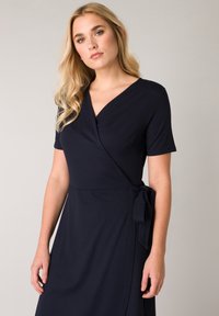 Navyblaues Wickelkleid aus weichem Stoff mit V-Ausschnitt, kurzen Ärmeln und einer gebundenen Akzentuierung in der Taille sowie einem fließenden Rock.