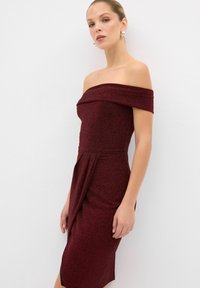 Burgundy off-the-shoulder mekko, joka on valmistettu rakenteellisesta kankaasta. Mekossa on istuva malli, drapeerattu etuosa ja polvipituinen helma, jossa on sivuaukko.