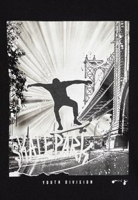 T-shirt noire avec un graphisme d'un skateur en plein trick, agrémentée d'une éclaboussure de peinture blanche et du texte "Division Jeunesse Skatepark."