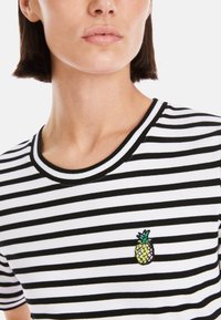 Black and white striped t-shirt with a round neckline and short sleeves, featuring a colorful embroidered pineapple design on the chest.