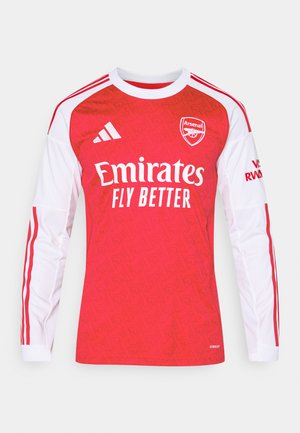 Red long-sleeve soccer jersey with white accents, featuring a textured pattern, logo on chest, and "Emirates" text. Three stripes on shoulders.