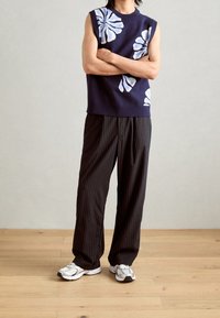 Granatowy bezrękawnik z białym kwiatowym wzorem, połączony z czarnymi spodniami w prążki i szarymi sneakerami, na jasnym tle.