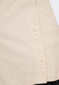 Μπεζ υφασμάτινη ριγωτή ύφανση με μια κάθετη σειρά από πέντε κουμπιά με τέσσερις τρύπες στην δεξιά ραφή ενός ενδύματος.