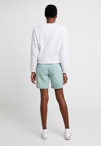 Vaaleanharmaa collegepaita, jossa on pyöreä pääntie ja raglan-hihat, yhdistettynä mintunvihreisiin shortseihin ja valkoisiin tennareihin.