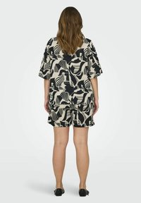 Ensemble noir et crème à motifs comprenant un haut ample et un short, avec des designs abstraits et des manches courtes. Chaussures plates noires.