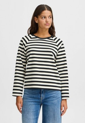 Zwart en crème gestreepte langemouwen top met een ronde halslijn en raglan mouwen. Gecombineerd met lichtblauwe spijkerbroek.