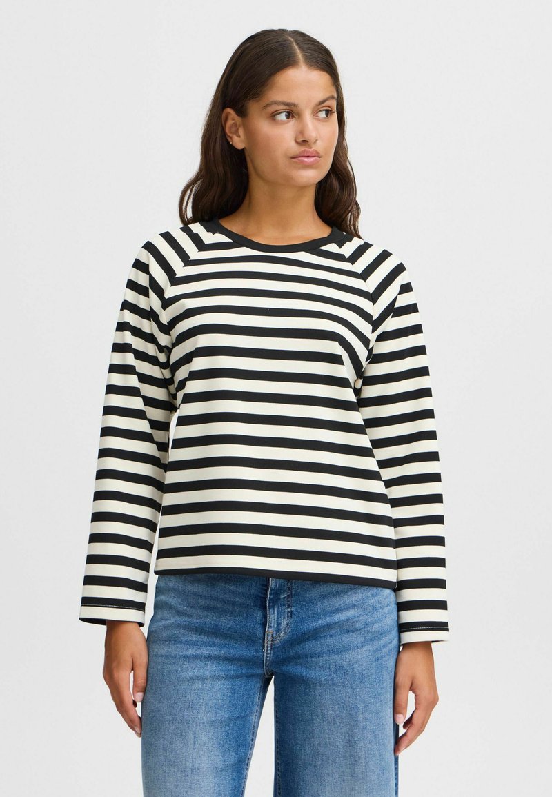 Black and cream striped long-sleeve top with a round neckline and raglan sleeves. Paired with light blue denim jeans.