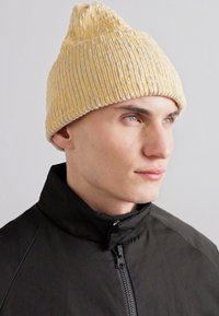 Kollane kudum peaksafari, millel on tekstuuriga ribakujundus ja terav kroon. Kandja on riietatud musta lukuga jope sisse.