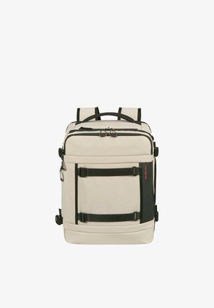Beige rectangular backpack with black straps and handles, front zipper pocket, and compression straps on sides and front panel.