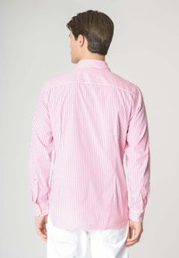 Camicia a maniche lunghe di un rosa chiaro con sottili righe bianche. Presenta un colletto con bottoni, polsini con chiusura a bottone e un orlo dritto.