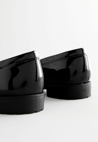 Mocassini in vernice nera con una finitura liscia, punta arrotondata e suole in gomma testurizzata. Presentano cuciture pulite e un design elegante.