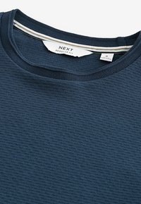 Diepblauwe gestructureerde sweater met een ronde halslijn, geribbelde manchetten en een gestreepte detail aan de binnenkant van de kraag. Merklabel "NEXT" zichtbaar.