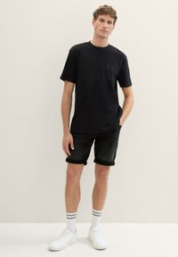 Czarny t-shirt z krótkim rękawem z kieszonką na piersi; połączony z czarnymi szortami z podwiniętymi nogawkami, białymi trampkami i paskowanymi białymi skarpetami.