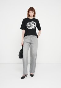 Black graphic t-shirt featuring a disco ball design, paired with light gray wide-leg jeans and black pointed-toe heels; holding a black bag.