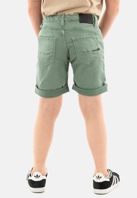 Pantalones cortos verdes con puños doblados en mezcla de algodón, que cuentan con bolsillos traseros y un acento con cremallera. Combinados con zapatillas negras y blancas.