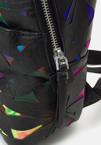 Mustan nahkarepun, jossa on värikkäitä geometrian muotoisia leikkuja, hopeinen vetoketjukiinnitys ja säädettävä musta hihna, tekstuuri pinta.