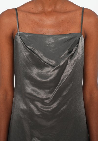 Woman wearing a sleeveless, shiny gray satin dress with thin straps and a draped neckline, shown from shoulders to mid-torso.
