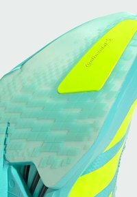 A close-up of a sneaker's sole features a translucent blue material with a bright yellow accent and textured grip pattern, including a logo.
