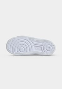 Λευκή σόλα παπουτσιού Nike με κυκλικά μοτίβα πρόσφυσης και μικρό λογότυπο Nike στο κέντρο σε απλό φωτεινό φόντο.