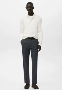 Weißes langärmliges Poloshirt kombiniert mit grauen, schlank geschnittenen Hosen. Das Outfit zeichnet sich durch einen klassischen Kragen und eine dezente Textur aus. Braune Schuhe runden den Look ab.