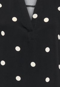 Tissu noir avec un col en V orné de grands pois blancs espacés uniformément sur la matière.