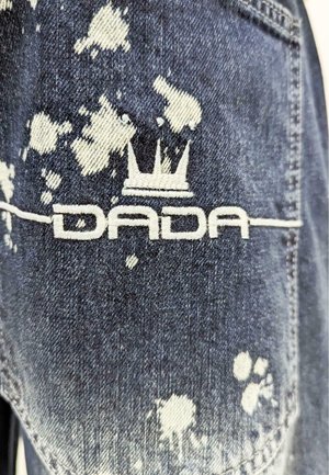 Denim jacket with a distressed finish, featuring white paint splatter, and an embroidered "DADA" logo with a crown icon in white.