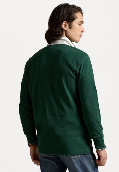 Groene blouse met lange mouwen van zachte stof, met een ronde hals en textuur. De achterkant toont een ontspannen pasvorm en ribgebreide manchetten.