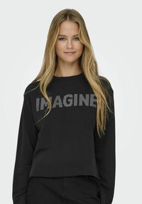 Sweatshirt croppat negru dintr-un material moale, cu cuvântul "IMAGINE" în strasuri argintii pe piept, decolteu rotund și mâneci lungi.