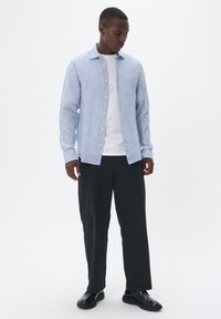 Camicia a righe blu e bianche, in cotone, con maniche lunghe e una consistenza morbida, abbinata a pantaloni neri e scarpe.