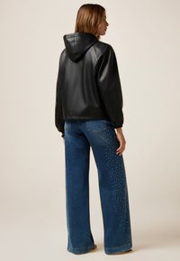 Zwarte nep leren jas met een capuchon, gecombineerd met blauwe wijde jeans met zilveren studs langs de zijnaad.