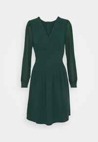 Grön klänning med långa genomskinliga ärmar, v-ringning och figurnära livstycke. Plisserad kjol och osynlig dragkedja bak. Slät tygtextur.