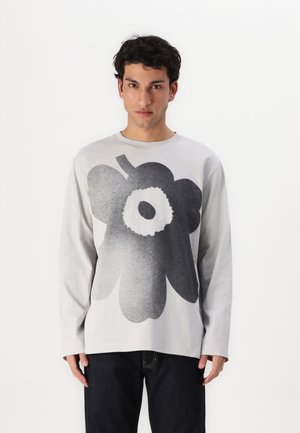 Szara koszulka z długim rękawem z dużym czarnym graficznym wzorem kwiatu, okrągłym dekoltem i miękkiego materiału bawełnianego, w komplecie z ciemnymi dżinsami.